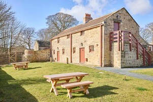 A stone building with a red door and a staircase. There are picnic tables in the foreground.