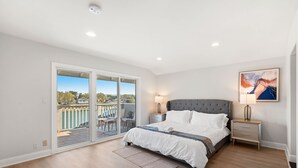 A bedroom with a large bed, a nightstand, a lamp, a painting, and a sliding glass door leading to a balcony. - Waterfront Retreat With Stunning Views Modern Co (Santa Ana)