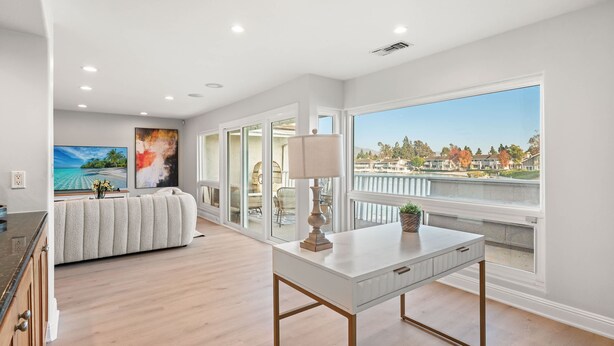 A spacious room with a large window, a white sofa, a dining table, and a painting on the wall. - Waterfront Retreat With Stunning Views Modern Co (Santa Ana)