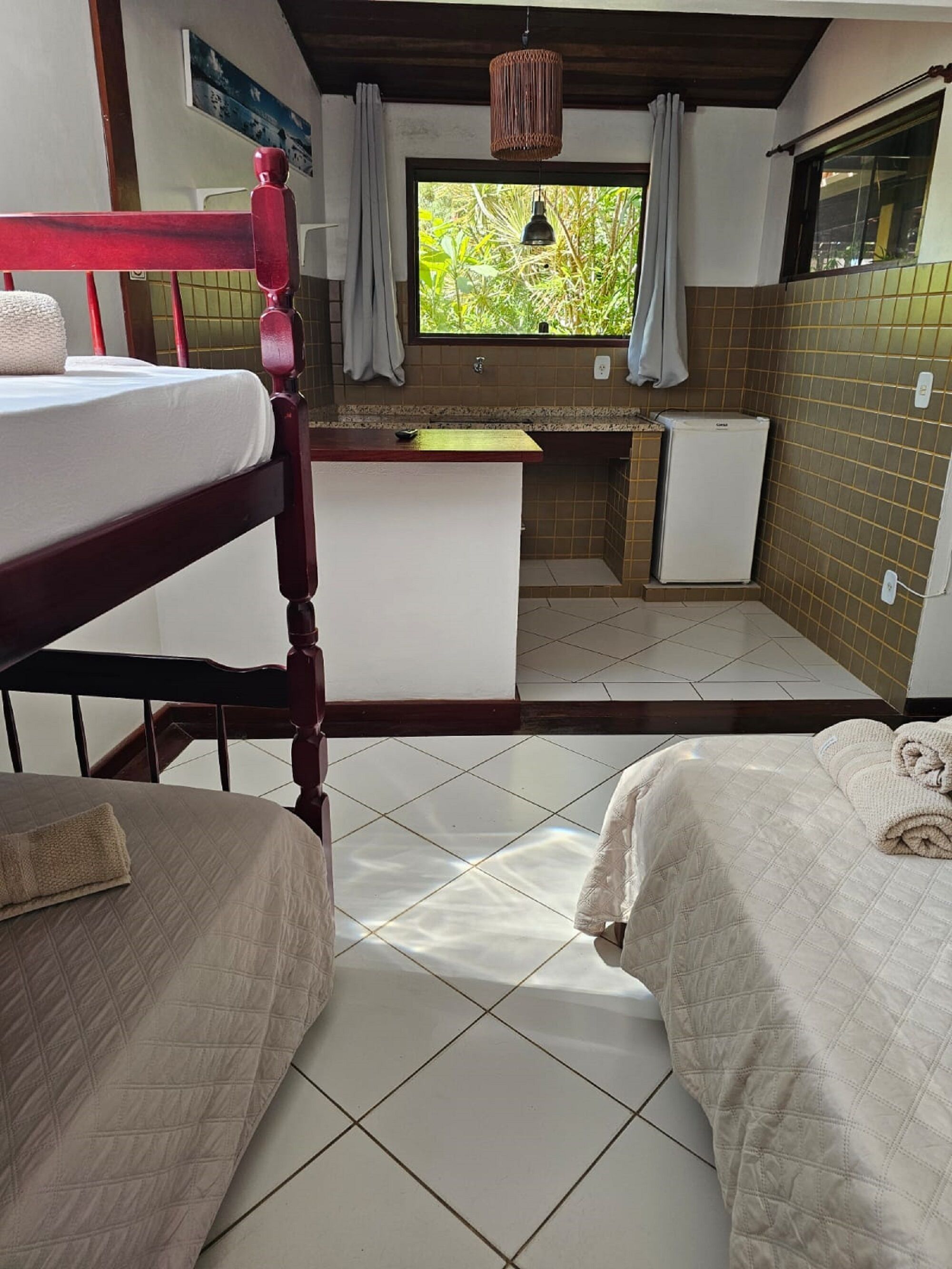 A compact room with two beds, a small kitchenette, and a window with a view of greenery.