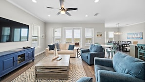 A spacious living room with a large TV, a ceiling fan, and a dining area with a view.