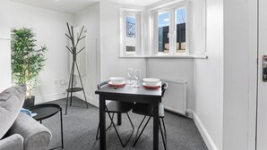 A modern, well-lit room with a dining table set for two, a grey sofa, a tall plant, and a black floor lamp. - The Hamlet - North East Escapes (North Shields)