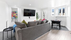 A modern living room with a grey sofa, a flat-screen TV, a dining table with chairs, and a radiator. - The Hamlet - North East Escapes (North Shields)