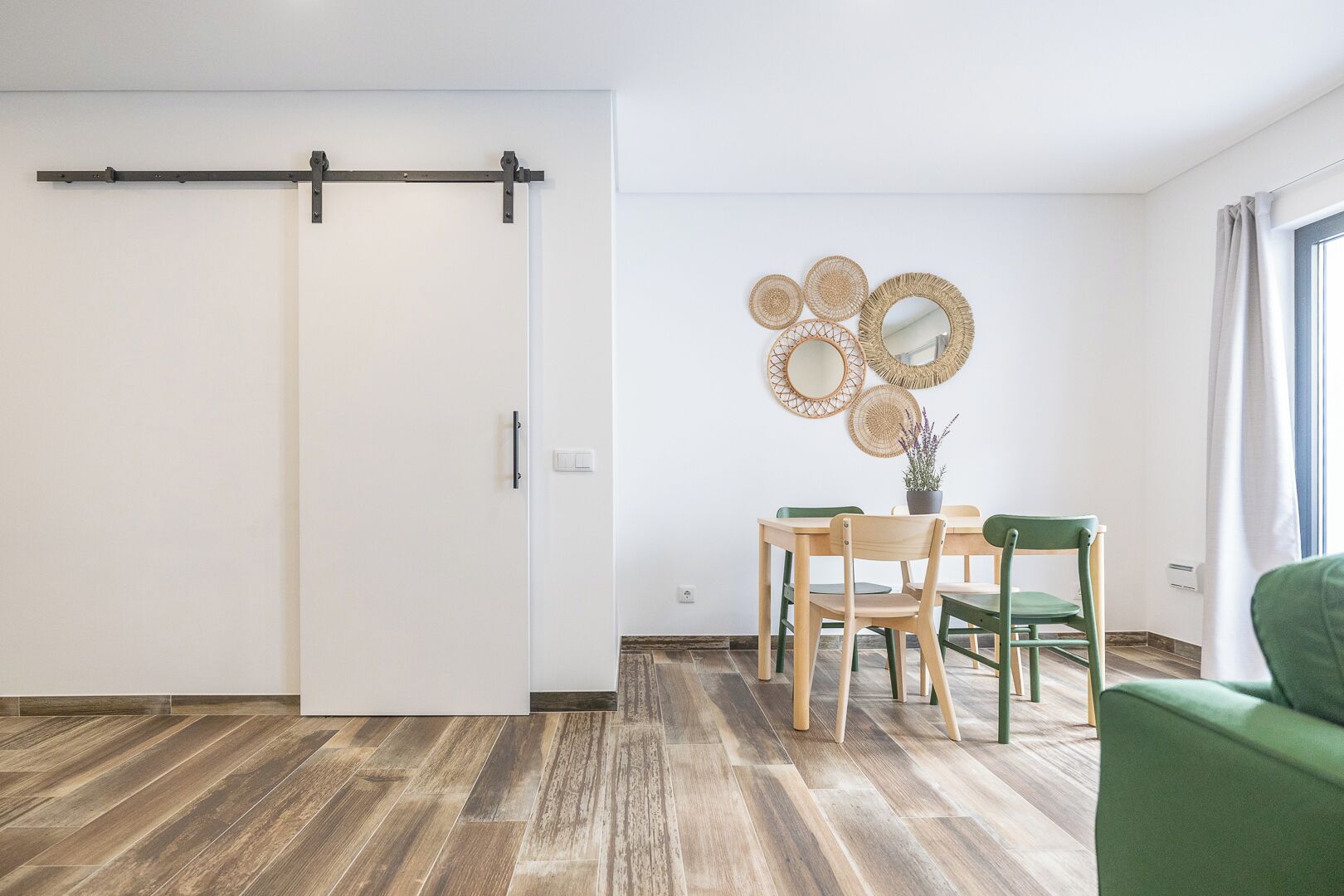 Ein Zimmer mit einer Schiebetür, einem Esstisch mit Stühlen, einem grünen Sofa und dekorativen Spiegeln an der Wand.
