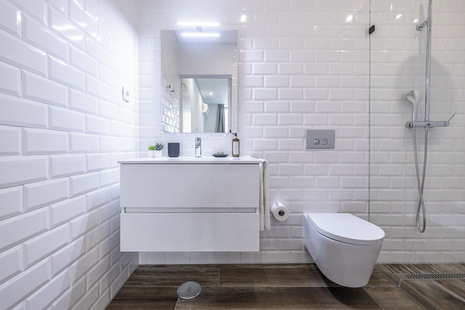 Ein modernes Badezimmer mit weißen Fliesen, einem weißen Waschtisch, einer Toilette und einer Duschkabine.