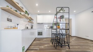 Una cucina moderna con mobili bianchi, scaffali in legno e un'isola centrale con sgabelli.