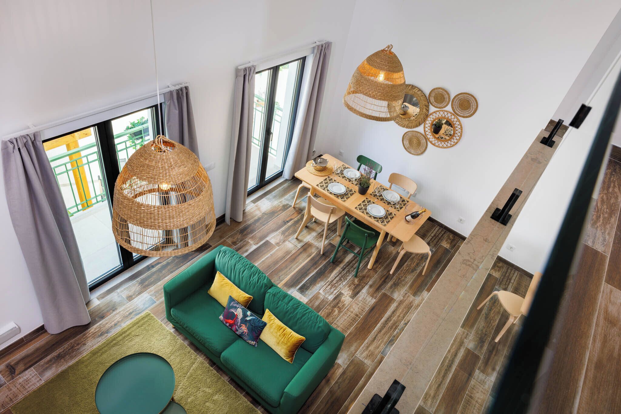 A modern living room with a green sofa, dining table, and a hanging wicker light fixture.