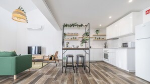Una cucina moderna con mobili bianchi, un piano di lavoro in legno e un forno integrato. C'è un'area pranzo con un divano verde e una TV.