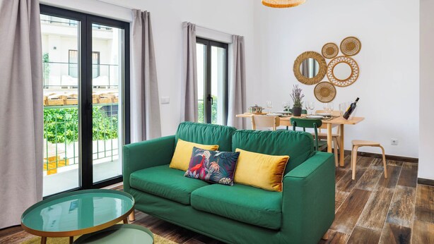 Un divano verde con due cuscini, un tavolino in vetro e un'area pranzo con tavolo e sedie.