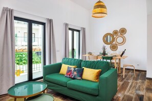 A green sofa with two cushions, a glass coffee table, and a dining area with a table and chairs.