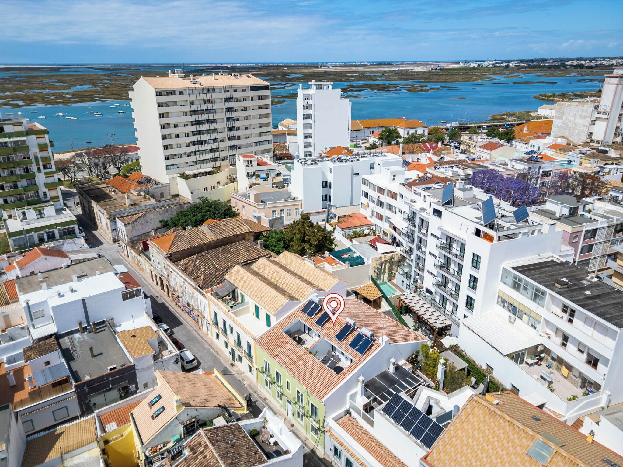 A coastal cityscape with a mix of modern and traditional architecture, including buildings with solar panels and a view of the sea.