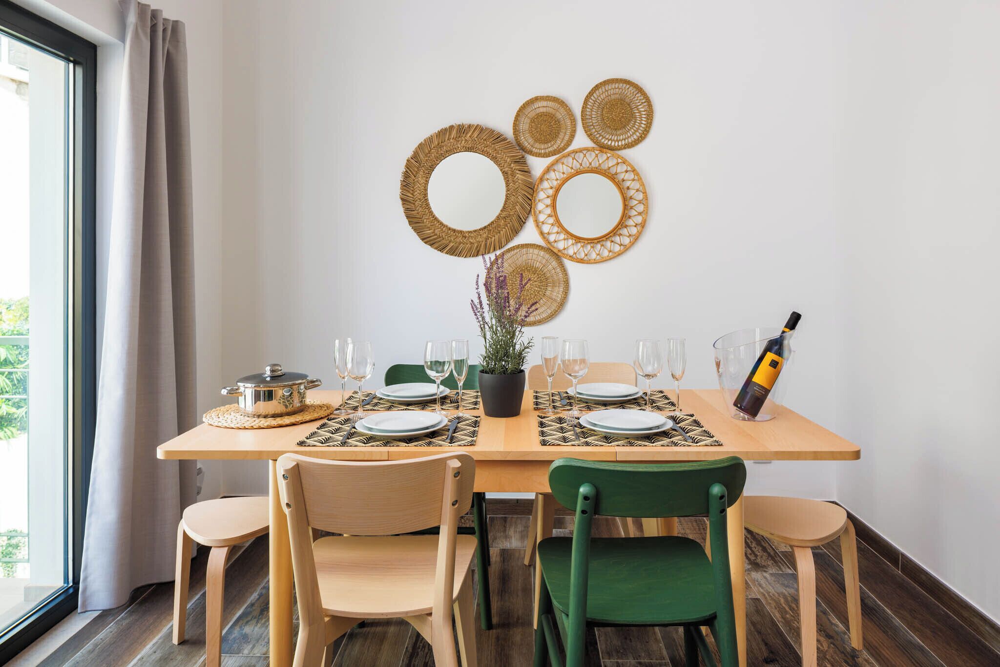A dining table set with plates, glasses, and a bottle of wine, surrounded by chairs.