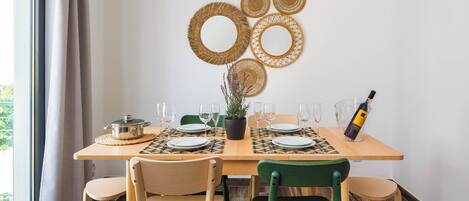 A dining table set with plates, glasses, and a bottle of wine, surrounded by chairs.