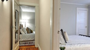 Een smalle gang die leidt naar een slaapkamer met een bed, een nachtkastje en een lamp.
