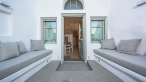 A modern interior with a central doorway leading to a dining area, flanked by two seating areas with cushions. - Cave Villa Valente (Santorini)