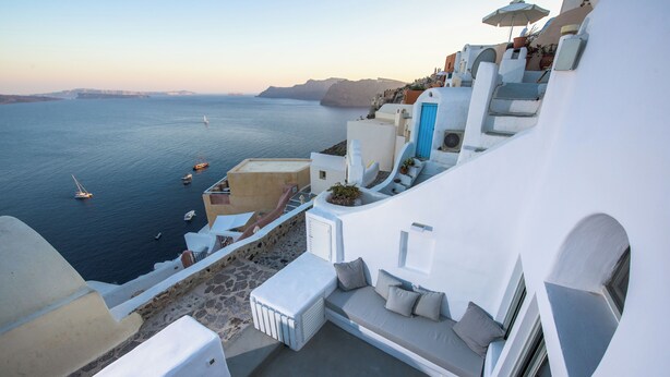 A white building with a balcony overlooking the sea, featuring a sofa and a radiator. - Cave Villa Valente (Santorini)