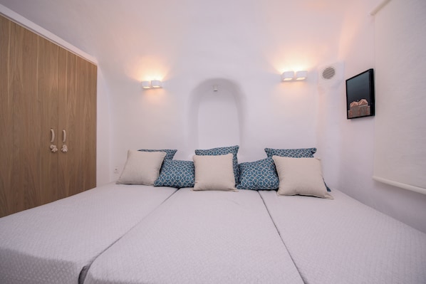 Un dormitorio con cama, almohadas, un armario e iluminación en la pared.