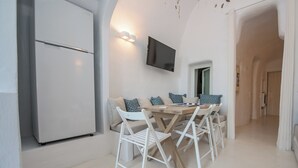 A modern kitchen with a built-in refrigerator, a dining table with chairs, and a flat-screen TV mounted on the wall. - Cave Villa Valente (Santorini)