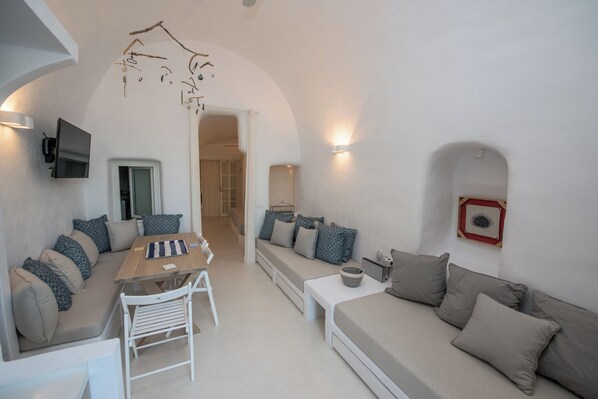 A modern living room with a sofa, a dining table, and a TV mounted on the wall.