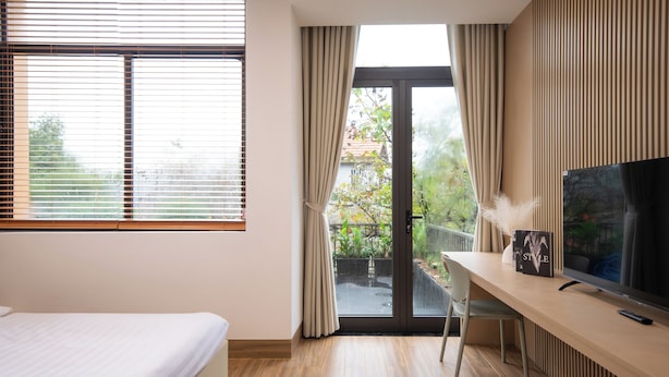 A hotel room with a bed, a desk with a TV, and a sliding glass door to a balcony. - Teky House 2 (Hue)
