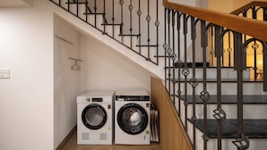 A laundry area with two washing machines and a staircase with ornate metal railings. - Teky House 2 (Hue)