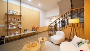 A modern living room with a staircase, white furniture, and decorative items on shelves. - Teky House 2 (Hue)