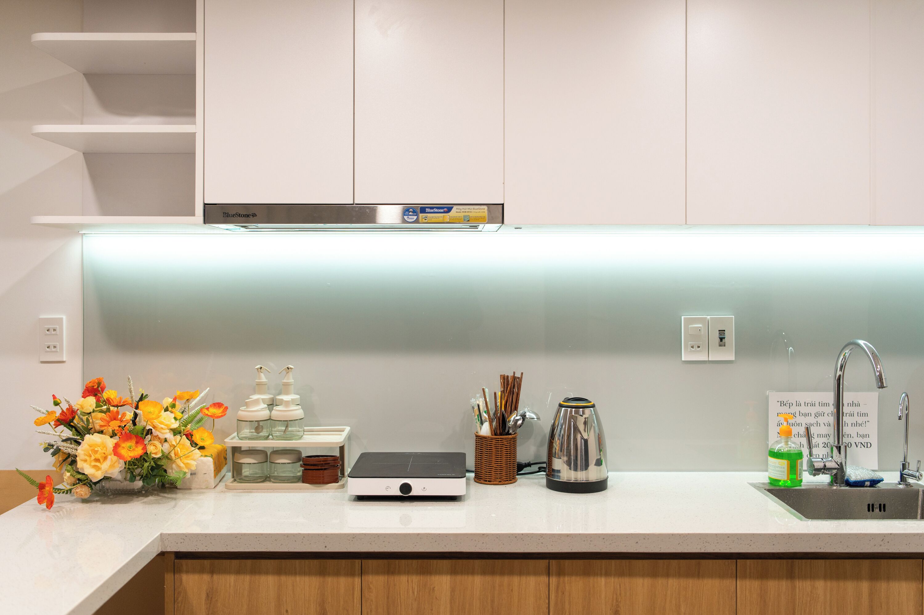 A modern kitchen with white cabinets, a built-in microwave, a kettle, and a sink with a faucet.