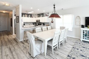 Een moderne keuken met witte kasten, een groot eiland met stoelen en een hangende hanglamp.