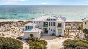 A beachfront property with a large house featuring multiple levels, a covered porch, and a view of the ocean.