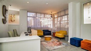 A modern living room with a white reception desk, yellow and blue armchairs, a coffee table, and a large window with sheer curtains. - 9 On Barrack (Cape Town)
