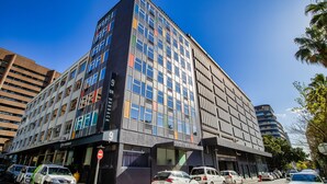 A modern multi-story building with a mix of glass and metal facade, several parked cars, and a clear blue sky. - 9 On Barrack (Cape Town)