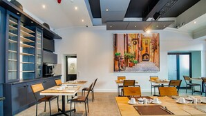 A modern dining area with tables set for breakfast, a large painting of a street scene on the wall, and a kitchen area with cabinets and a microwave. - 9 On Barrack (Cape Town)