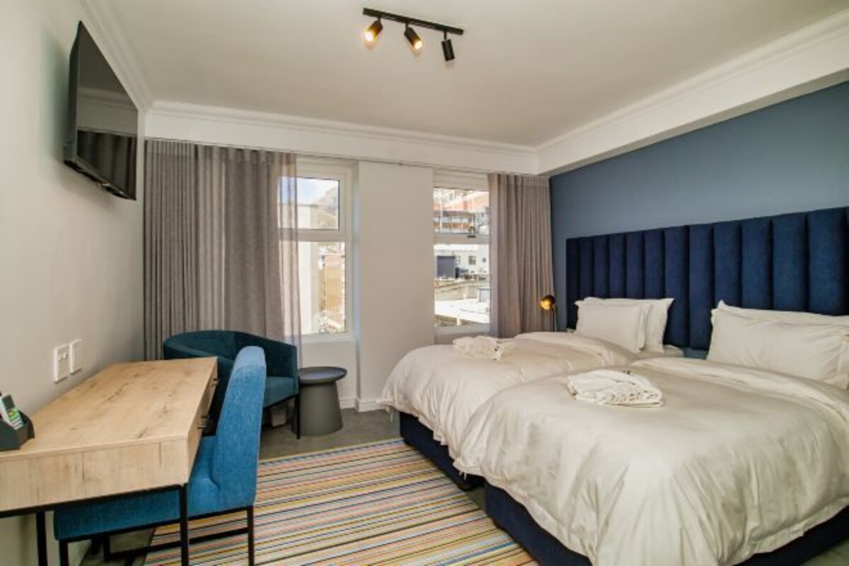 A hotel room with a bed, a desk, a chair, and a TV mounted on the wall.