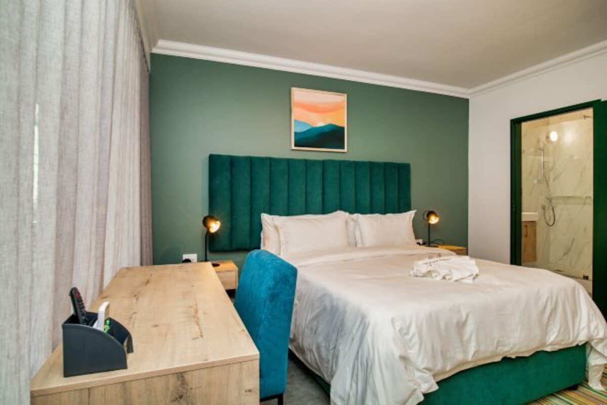 Hotellihuone, jossa on sänky, työpöytä, tuoli, taulu seinällä ja kylpyhuoneen ovi.