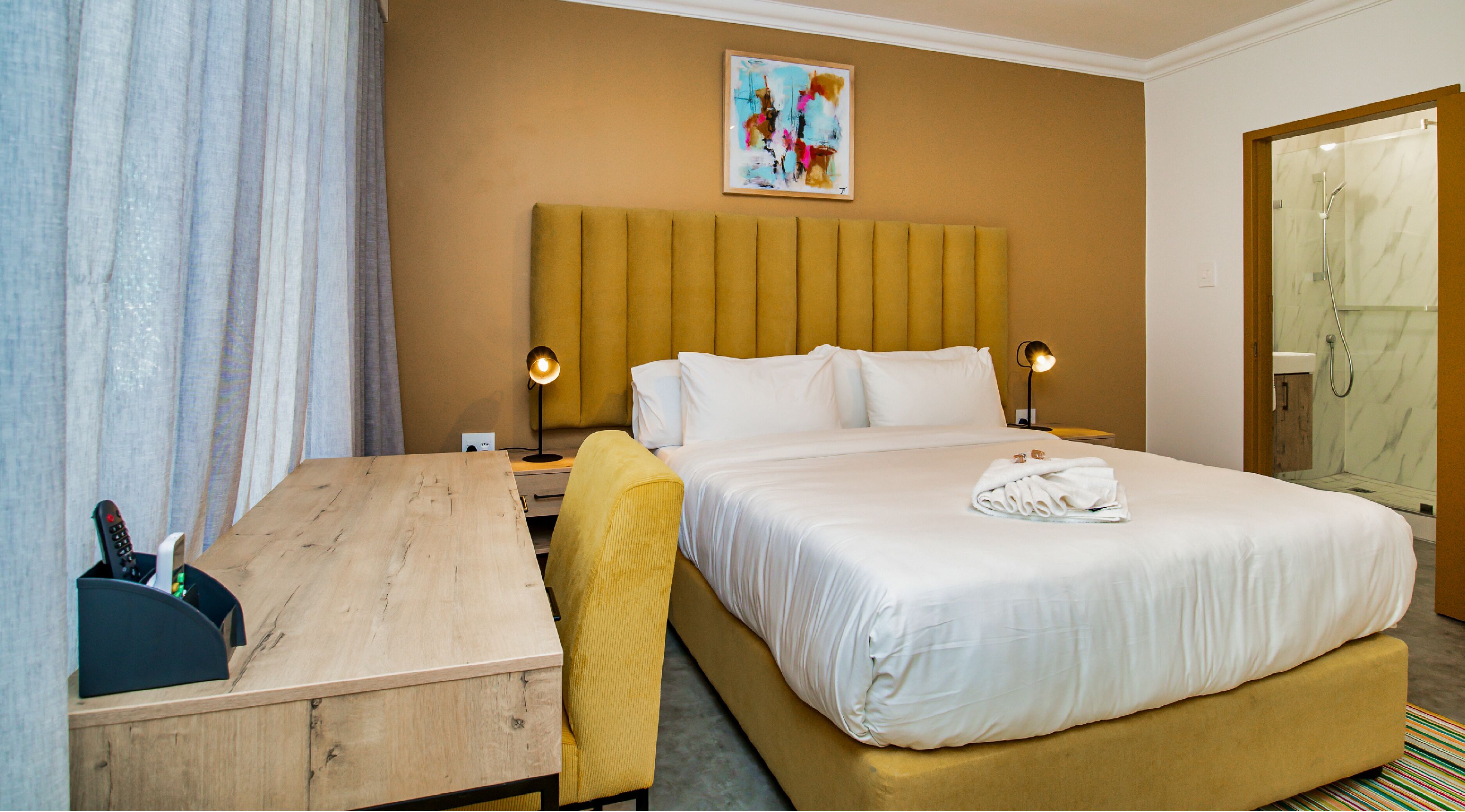 Una habitación de hotel con cama, lámparas de noche, escritorio, silla y zona de ducha.