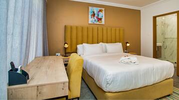 Una habitación de hotel con cama, lámparas de noche, escritorio, silla y zona de ducha.