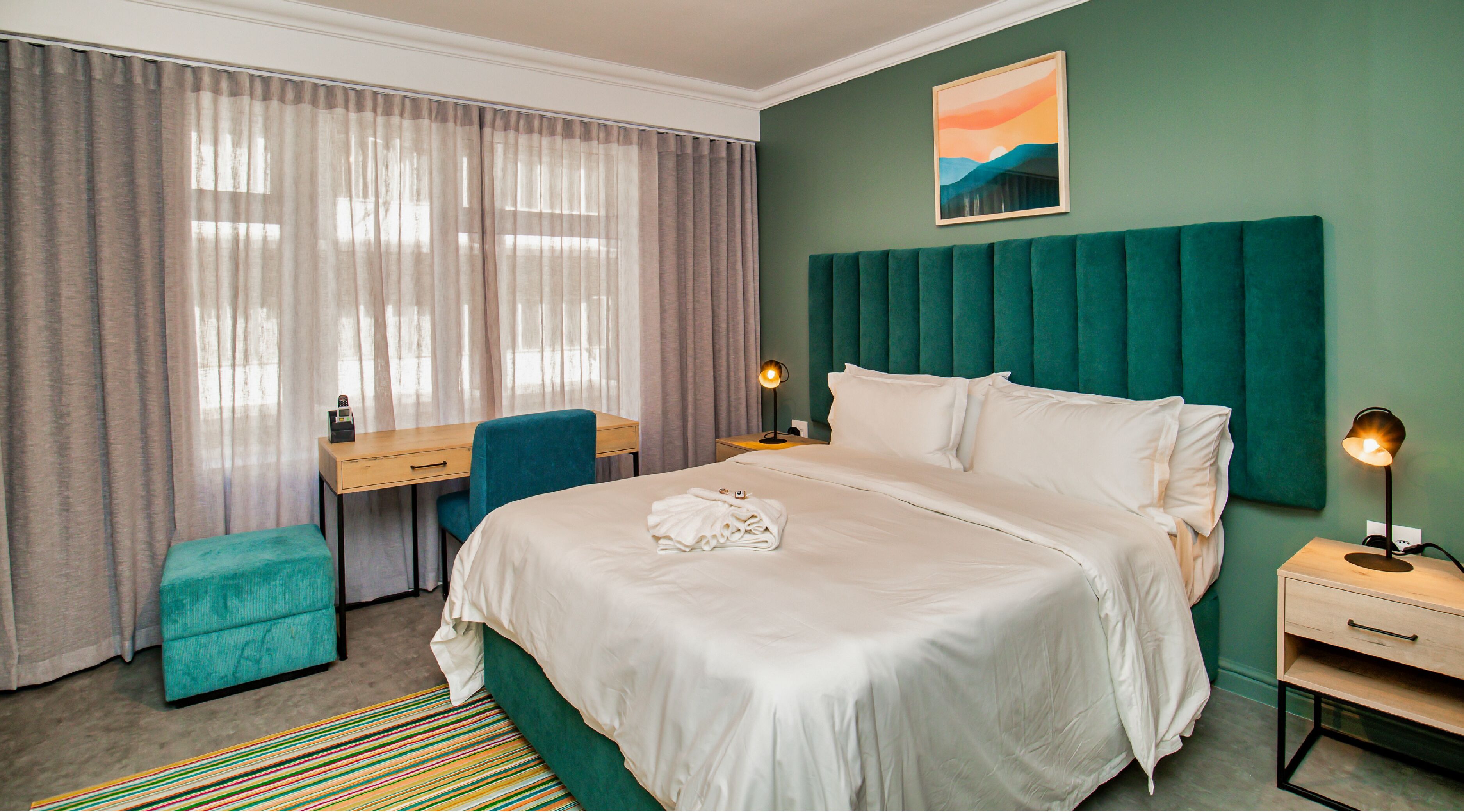 Habitación de hotel con cama, escritorio, silla y mesita de noche.