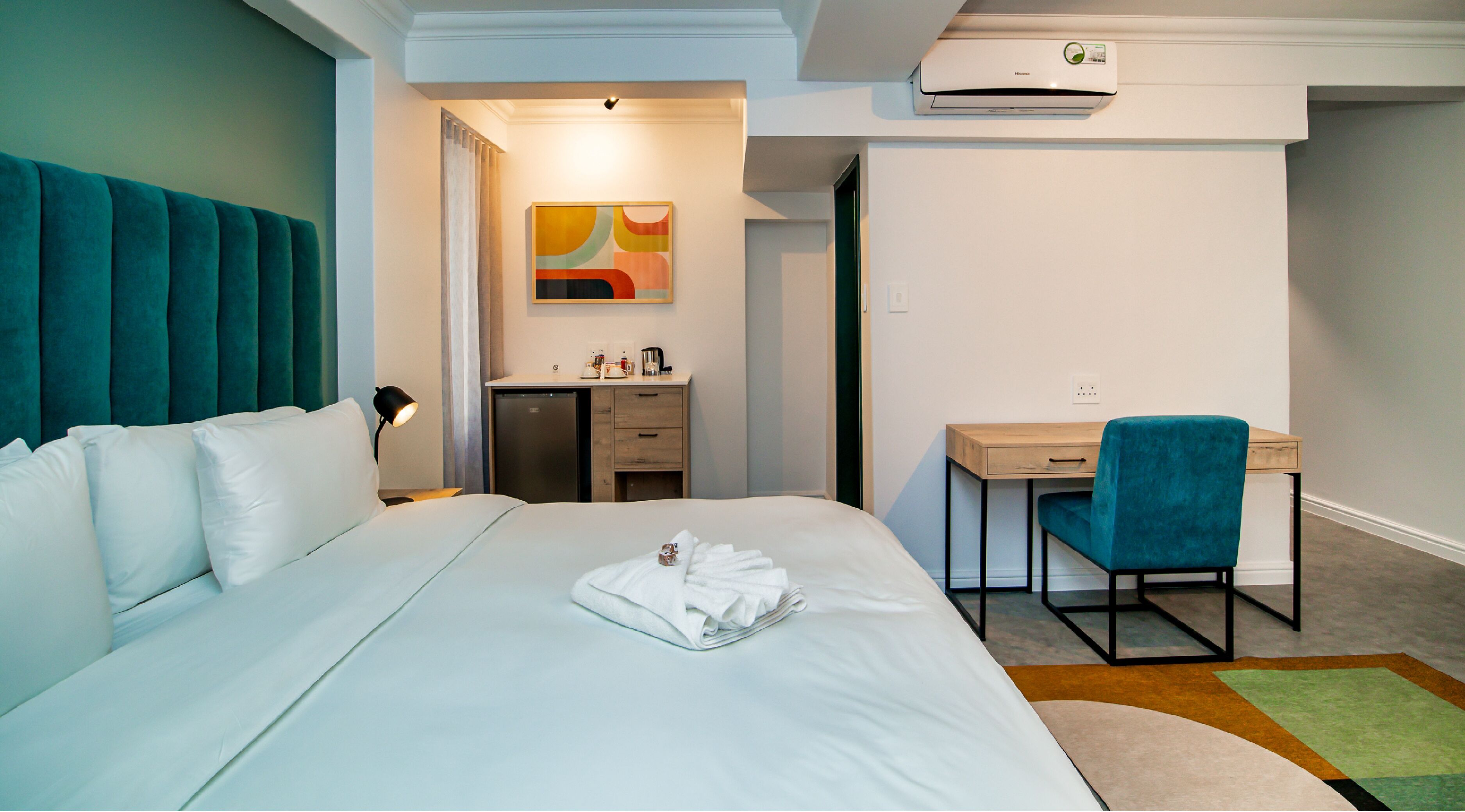 Habitación de hotel con cama, escritorio, silla, kitchenette pequeña y baño.