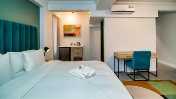 Habitación de hotel con cama, escritorio, silla, kitchenette pequeña y baño.