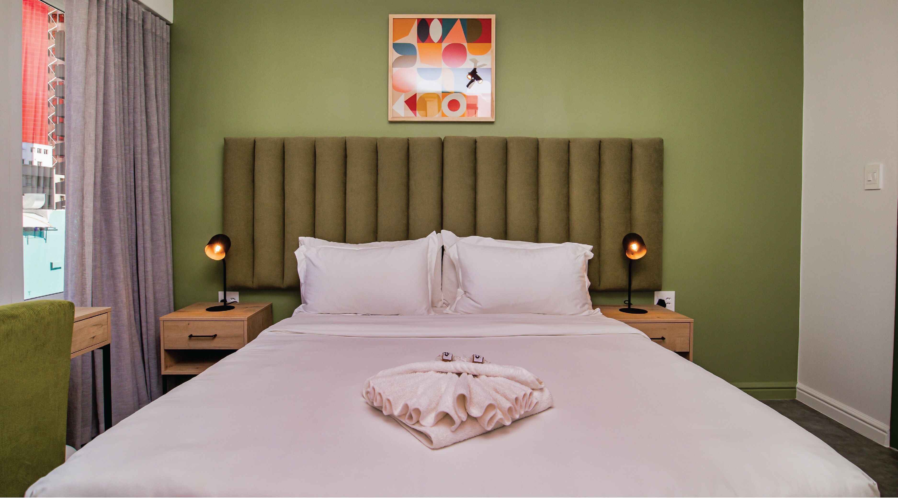 A hotel room with a large bed, two bedside tables, a headboard, and a painting on the wall.