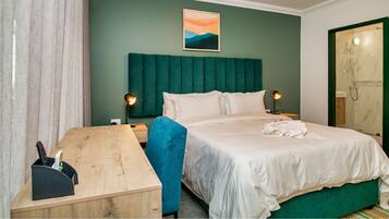 Habitación de hotel ordenada con cama, mesitas de noche, escritorio y zona de ducha.