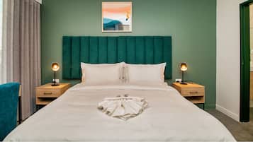 Quarto de hotel com uma cama grande, duas mesas de cabeceira com luminárias, cabeceira verde, um quadro na parede e vista para o exterior.