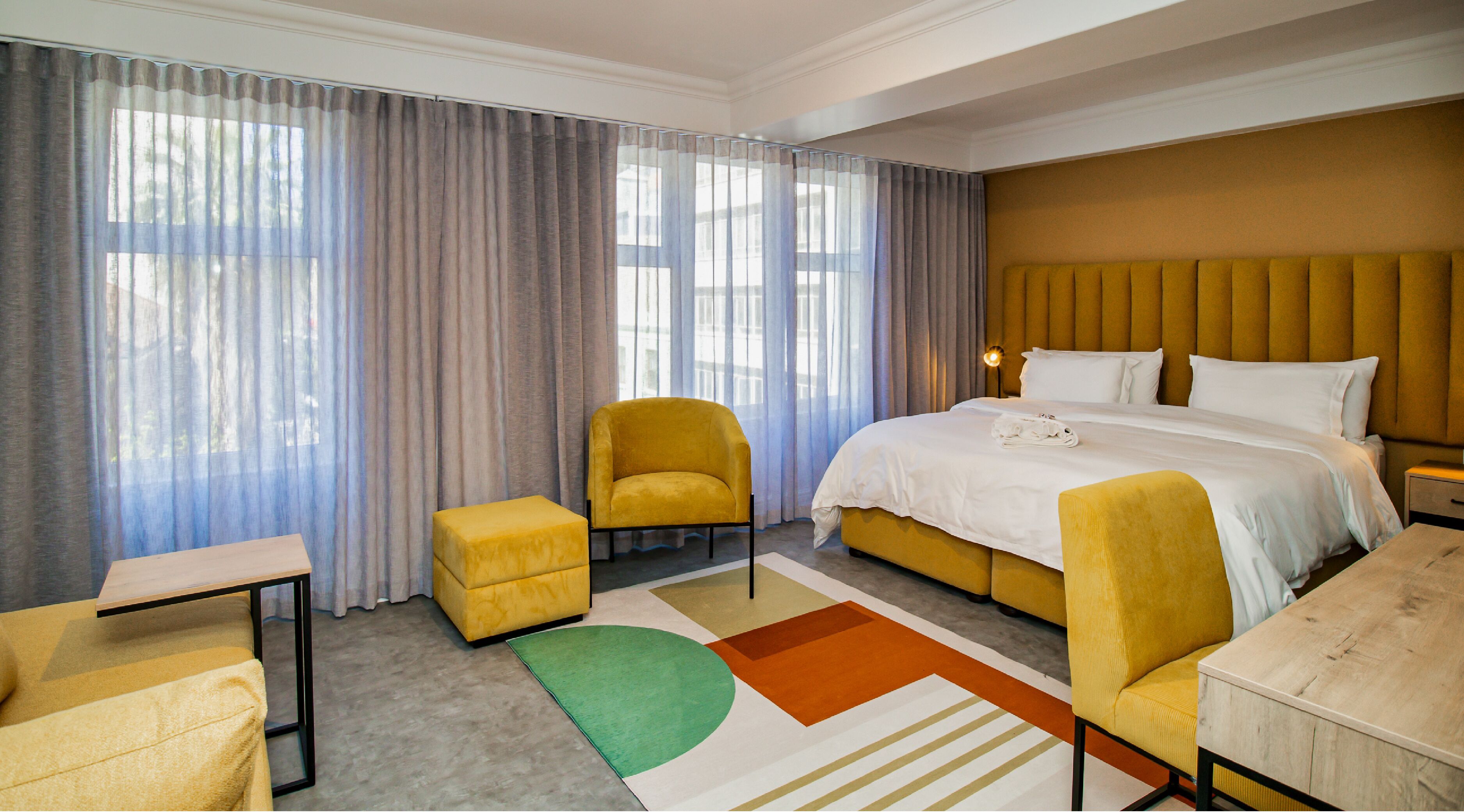 A hotel room with a large bed, a yellow armchair, a small table, and a green rug.