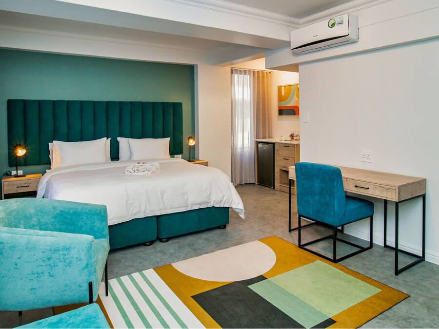 A hotel room with a bed, a desk, a chair, a bathroom, and an air conditioning unit.