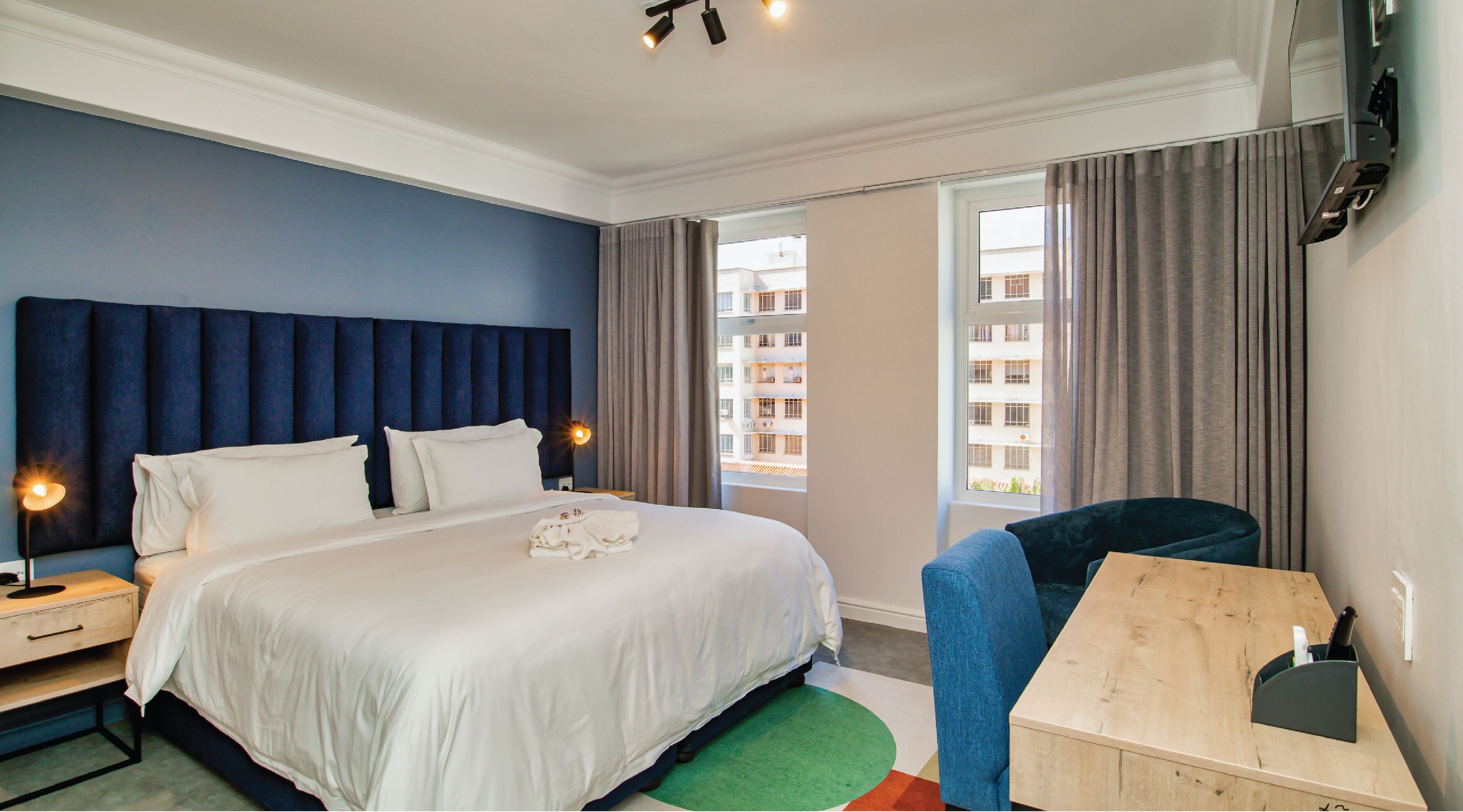 A hotel room with a large bed, a desk, and a view of buildings through the window.