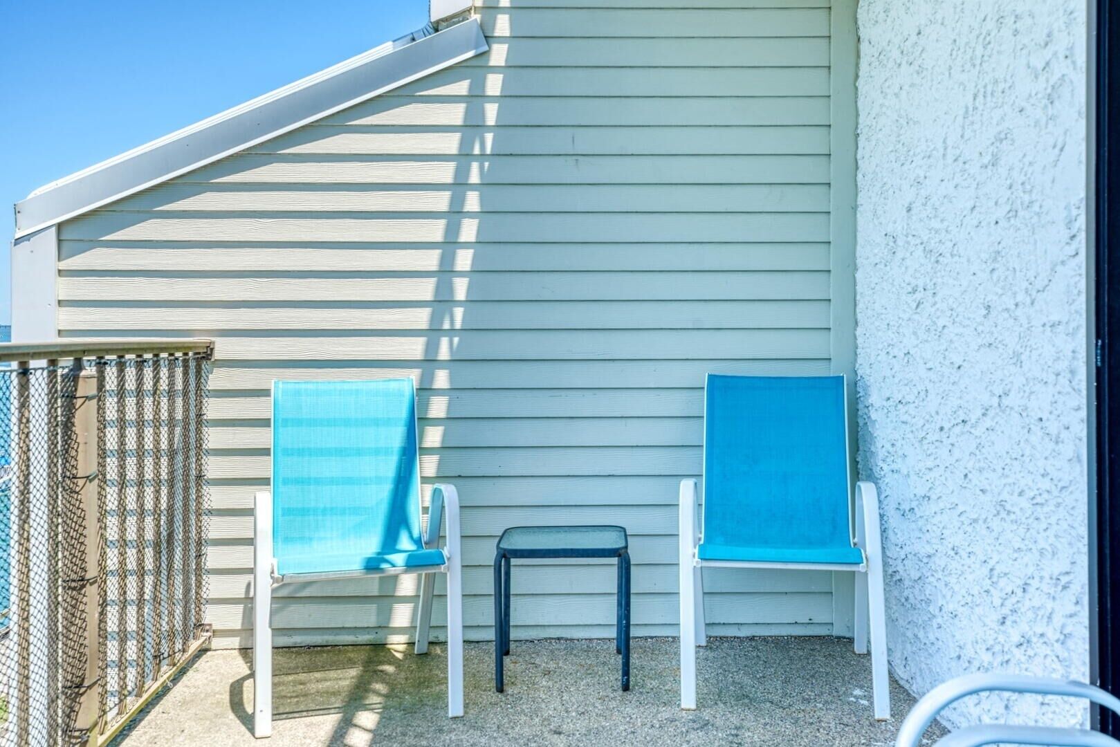 Zwei blaue Lounge-Stühle auf einer Schotterterrasse, im Hintergrund ein weißes Gebäude.