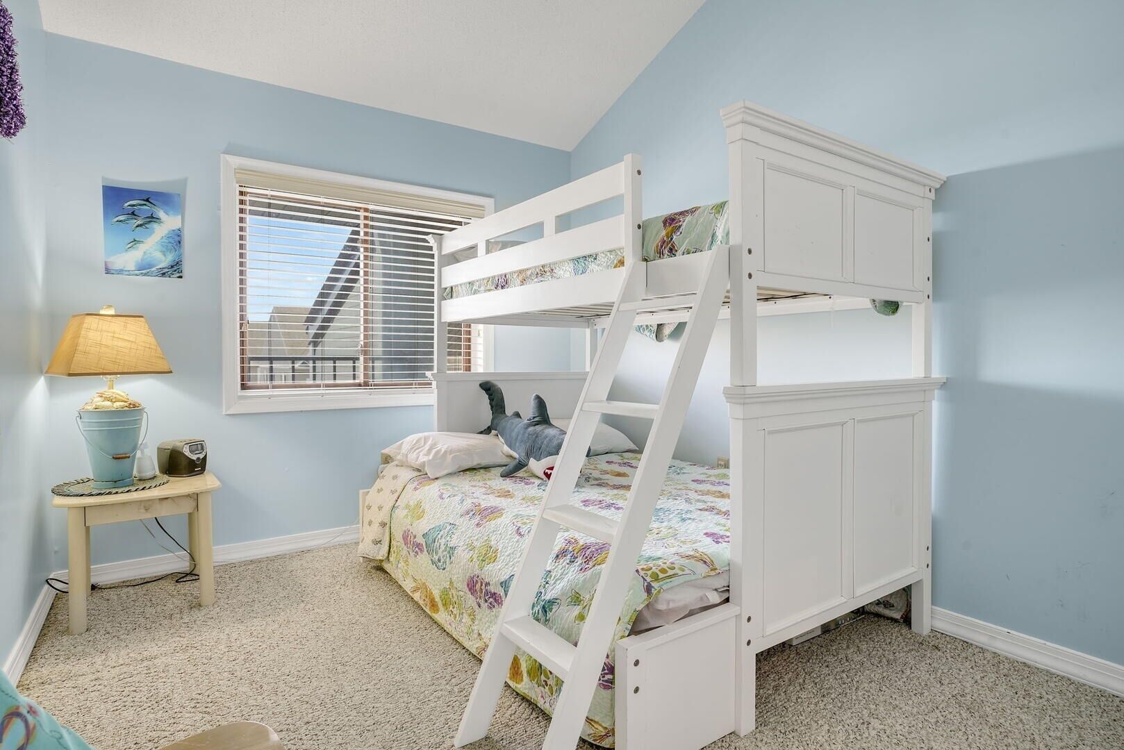 A bunk bed room with a window, a lamp, and a small table.