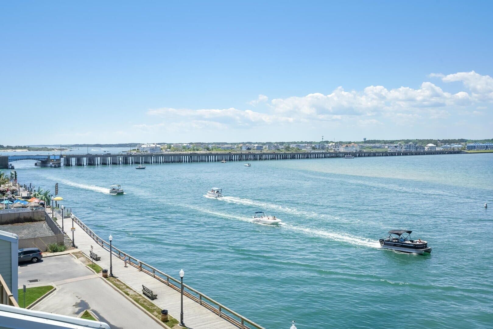 A waterfront promenade with a wooden walkway, boats, and a pier extending into the water.