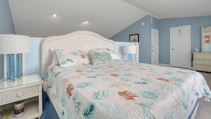 Quarto com cama, duas mesas de cabeceira, cômoda e uma porta.