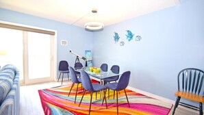 Uma sala de jantar com uma mesa de vidro, cadeiras azuis e um tapete colorido.